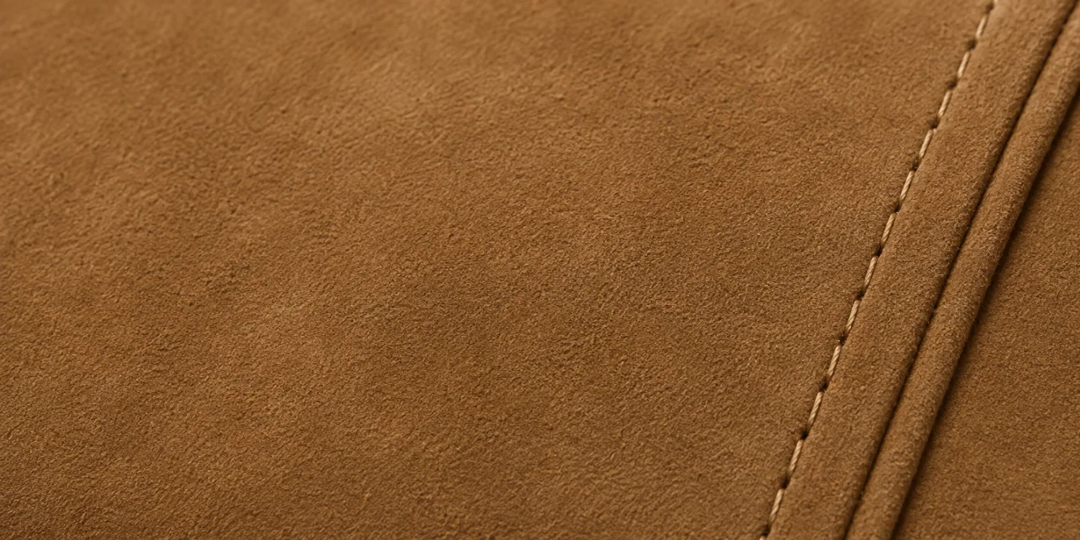 Macro of nubuck: the outer grain face sanded to a short, tight, even nap in warm tan, with two stitched seams running down the right side