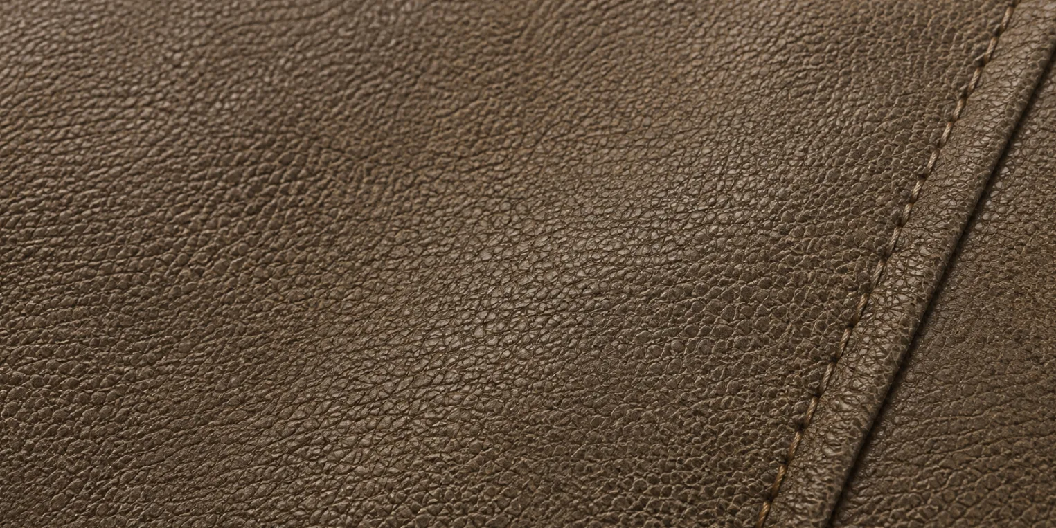 Macro of sueded leather: a grain hide brushed only lightly, so its pebbled grain pattern still reads clearly under a soft matte surface beside a stitched seam