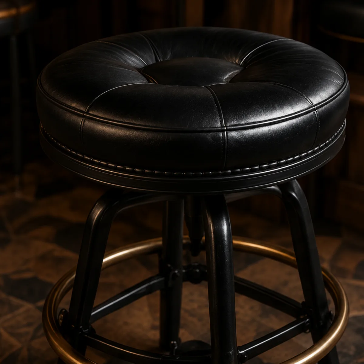 Black leather bar stool seat on a dark metal base with a brass footrail