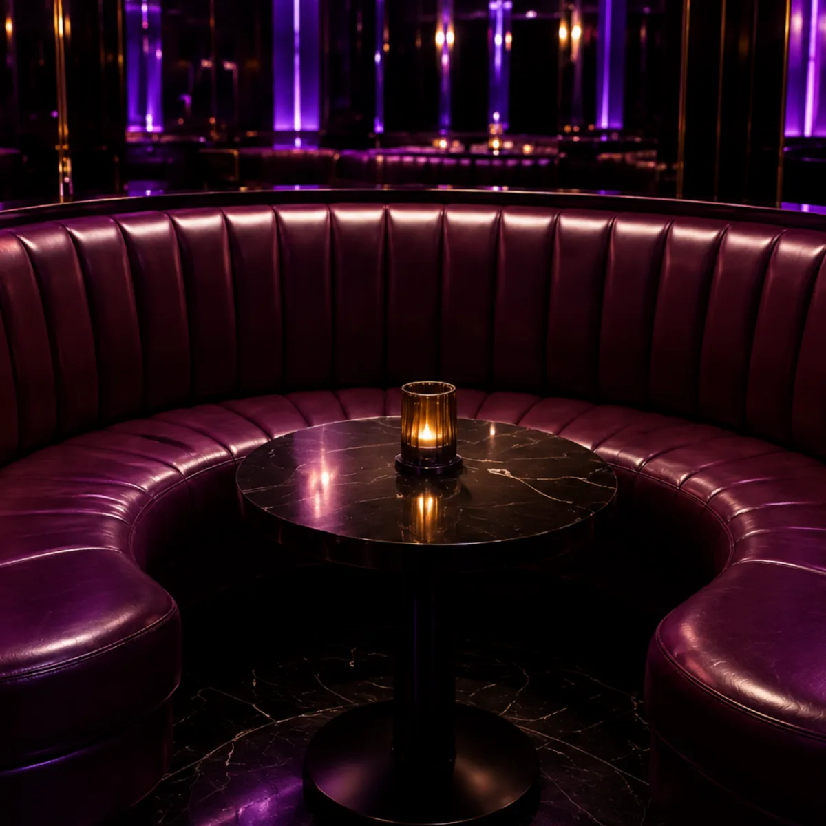 Curved oxblood leather VIP booth around a black marble table in a nightclub