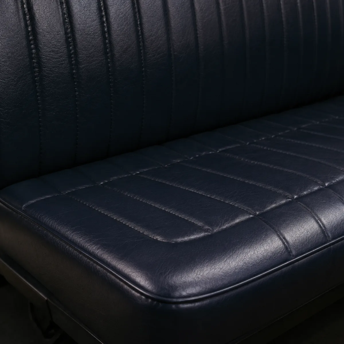 Restored dark navy fluted vinyl bench seat in a bus, even matte finish across the cushion and backrest