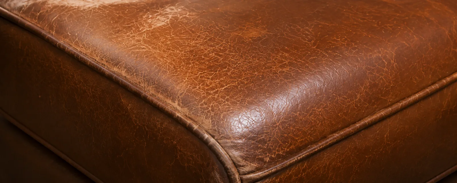 Crazed, lifting finish across the front edge of a tan top-grain leather seat cushion