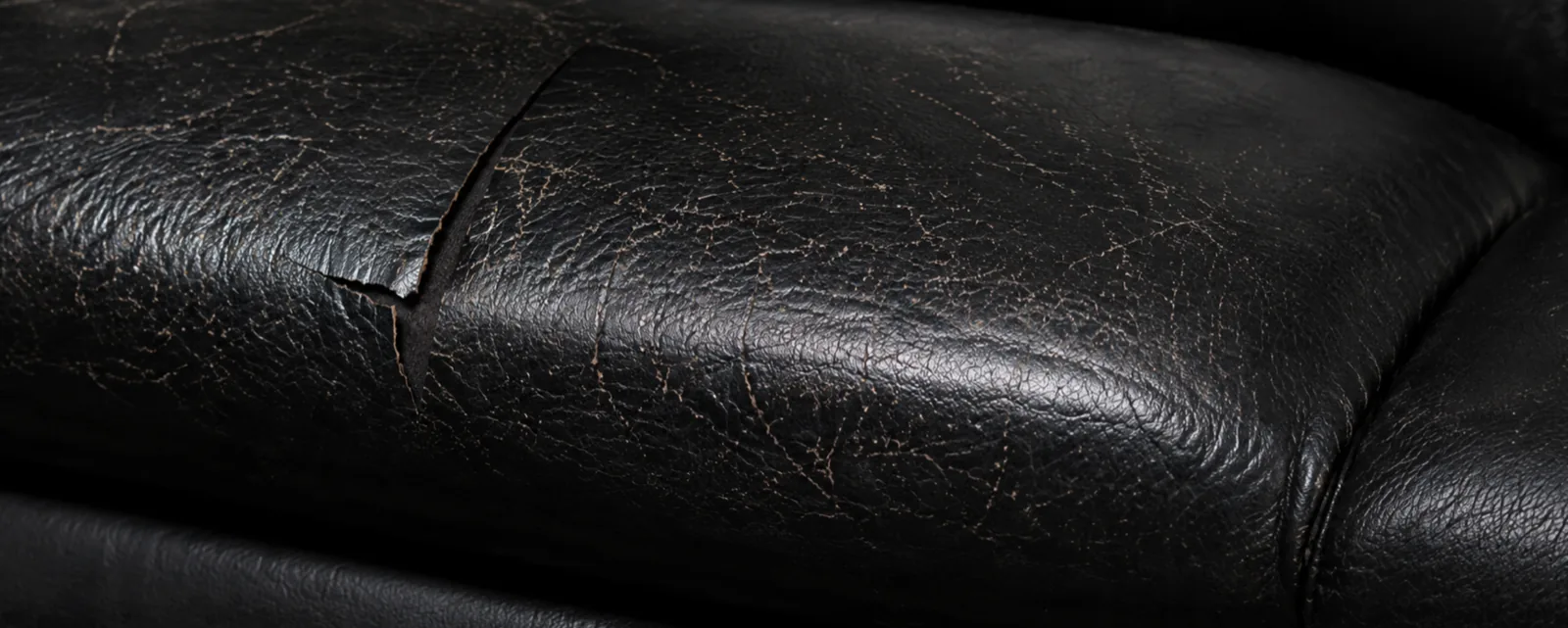 Deep cracking and a split running across a black top-grain leather seat panel