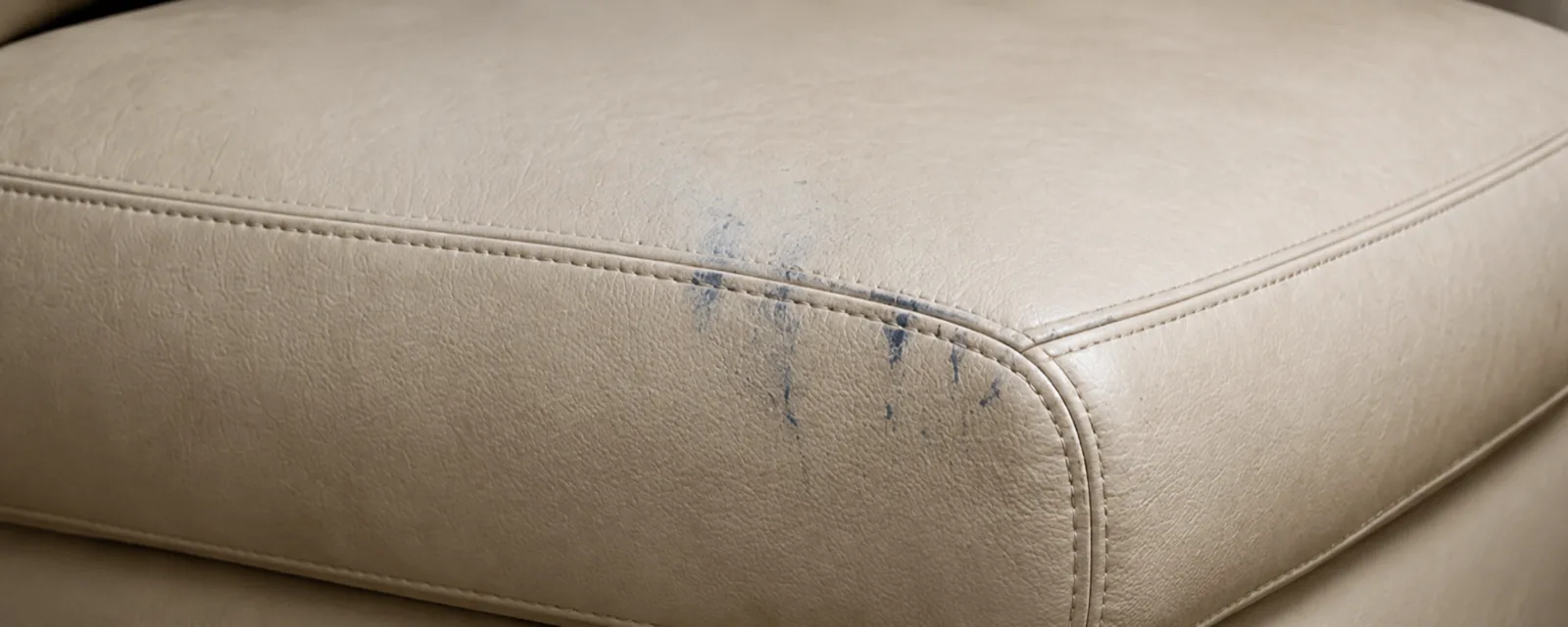 Blue ballpoint ink marks across the front edge of a cream leather cushion