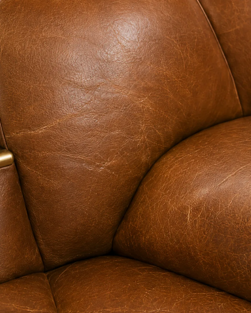 Aged top-grain leather armchair with the finish thinning and the colour lifting along the seat and arm creases