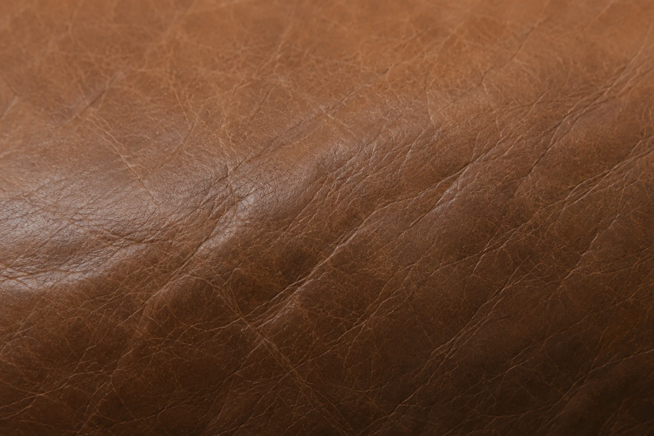 Brown semi-aniline leather reading light in one area and deeper in another, the tone shifting across the panel where the finish has worn unevenly