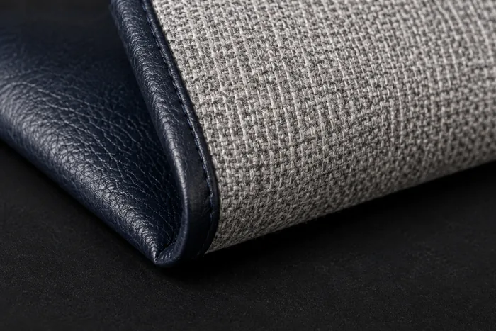 A navy vinyl folded back on itself to show its reverse, a pale grey woven fabric backing with a clear repeating basketweave grid