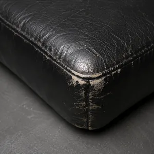 The stitched corner of a black vinyl seat worn pale and rough where it has rubbed repeatedly against something