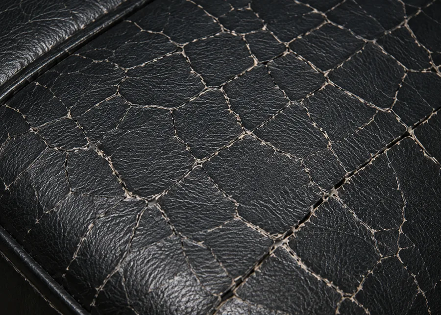 A black vinyl seat panel covered edge to edge in a fine web of cracks, the surface dulled and hardened with the pale backing showing through the deepest lines