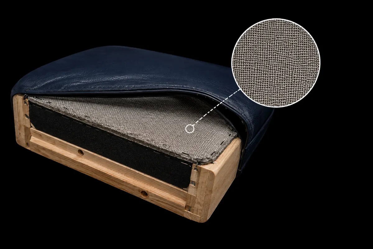 Vinyl vs leather test — a navy upholstered seat cushion turned over on its timber frame, the underside showing a pale woven fabric backing, with a magnified inset of that weave