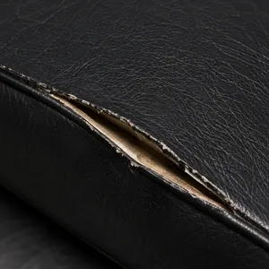 A black vinyl seam split open along the stitch line, the two edges parted to show pale backing beneath