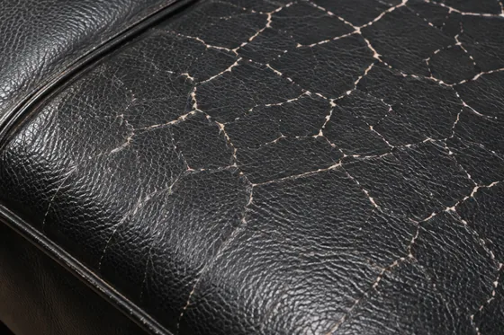 A close view of the worst-cracked area of the same sofa, the crack network filling the frame beside a piped seam