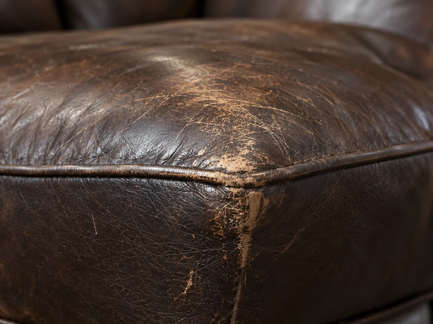 A dark brown ottoman with the surface finish abraded away along the crest