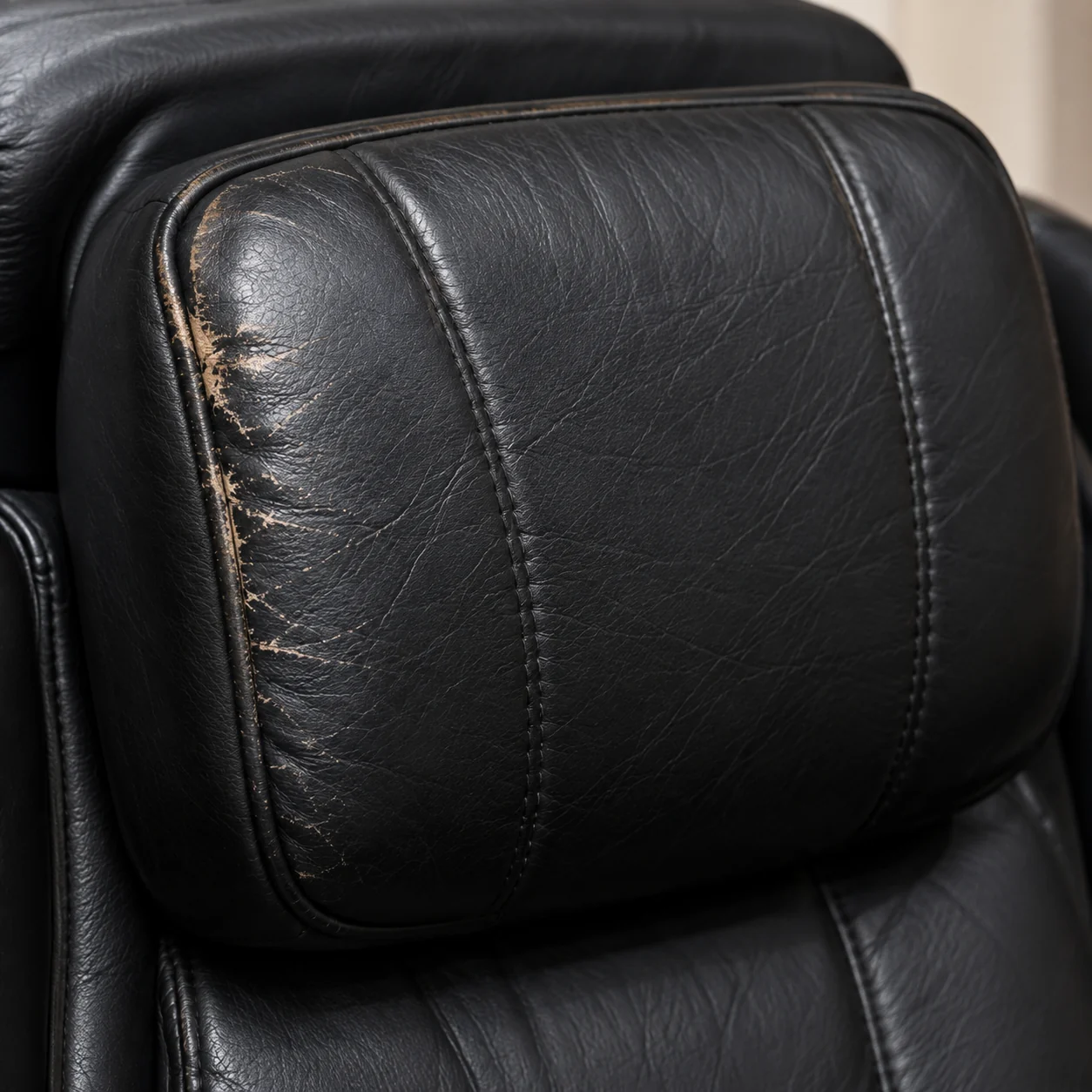 Abraded leather on the headrest pillow of a black massage chair, worn through to a tan layer