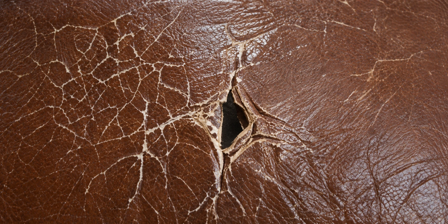 A network of cracks in brown leather opening into a hole