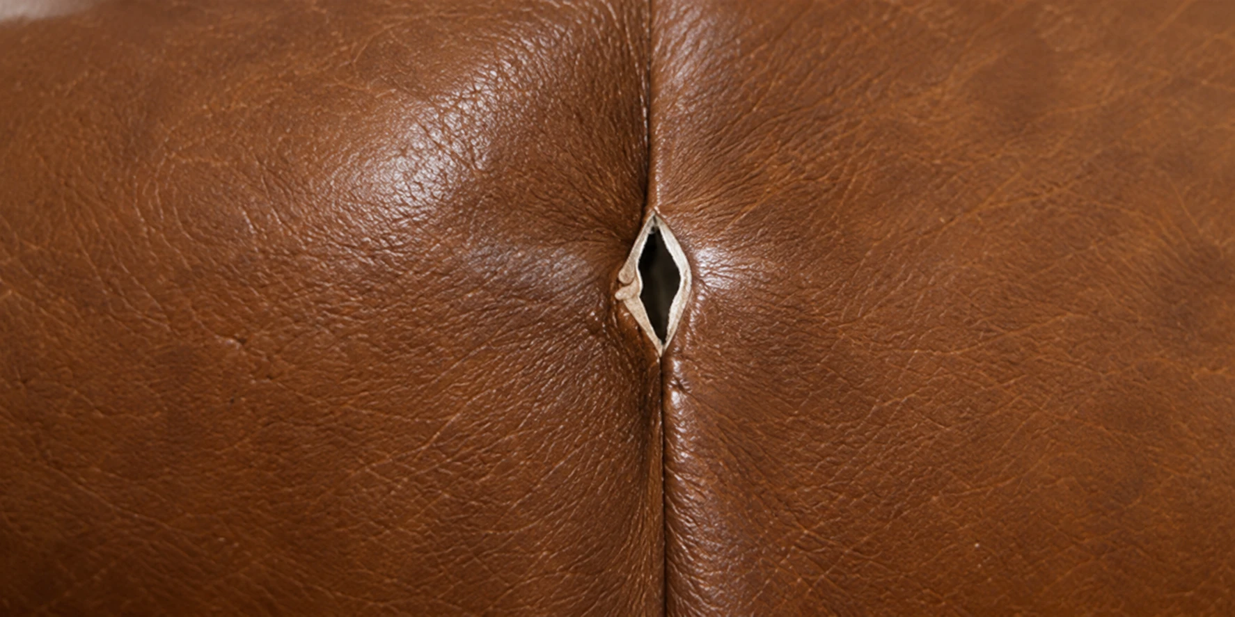 A small diamond-shaped tear opening along a seam on brown leather
