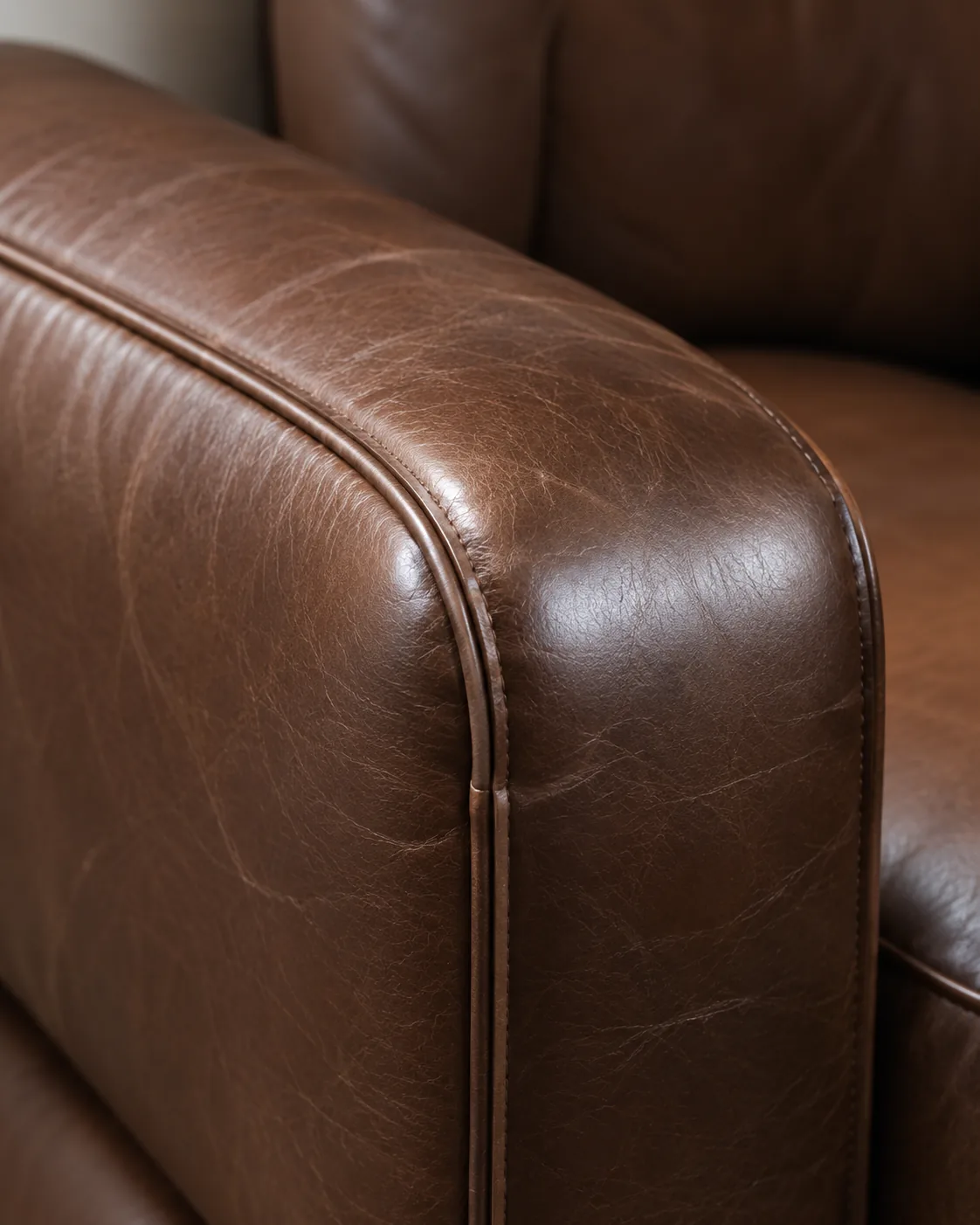 The piped brown leather arm of a classic sofa