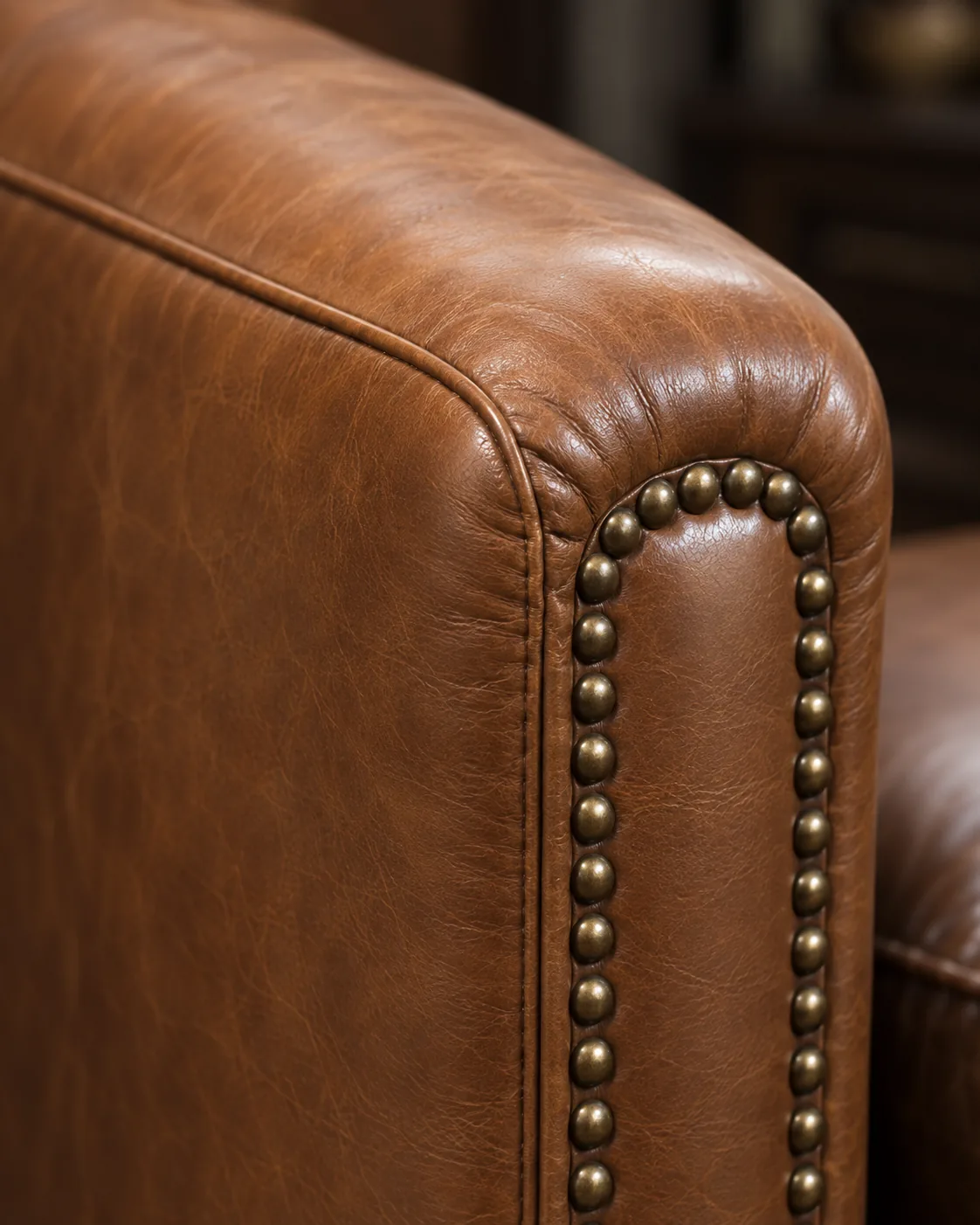 A tan club chair arm trimmed with brass nailheads