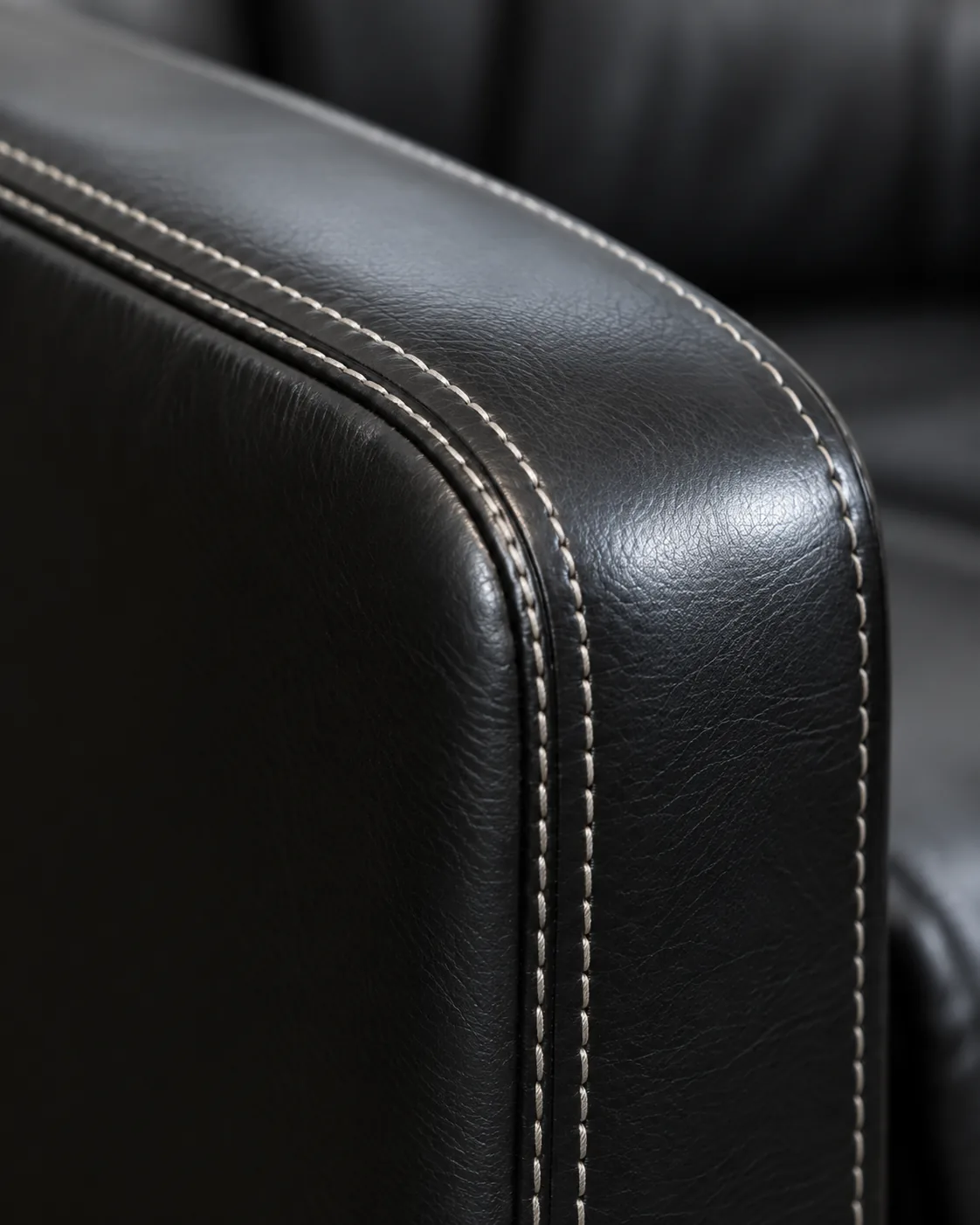 A black office chair arm with cream contrast stitching