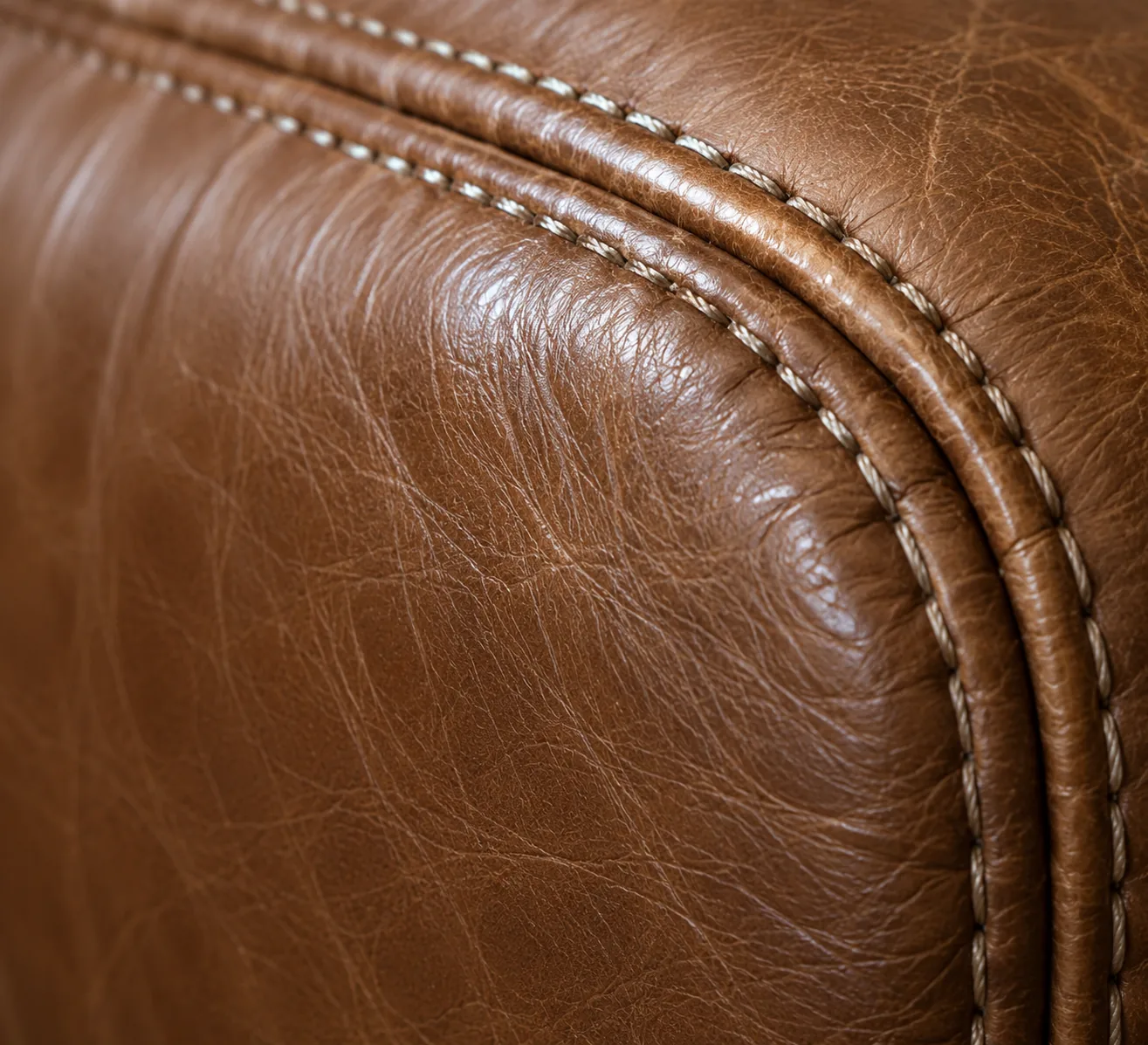 Contrast stitching running along the rolled edge of a brown leather arm