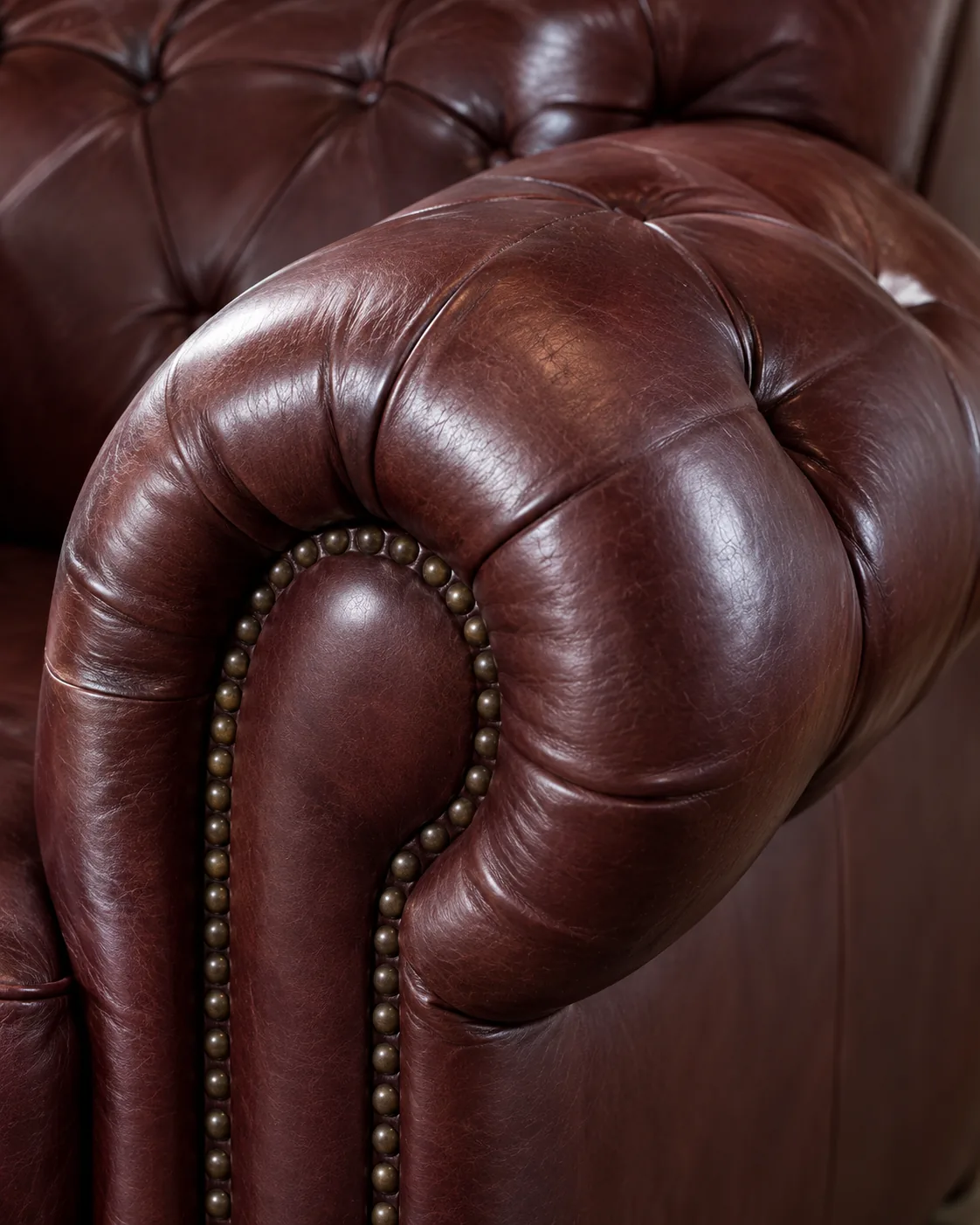 A buttoned burgundy tufted arm with brass nailhead trim