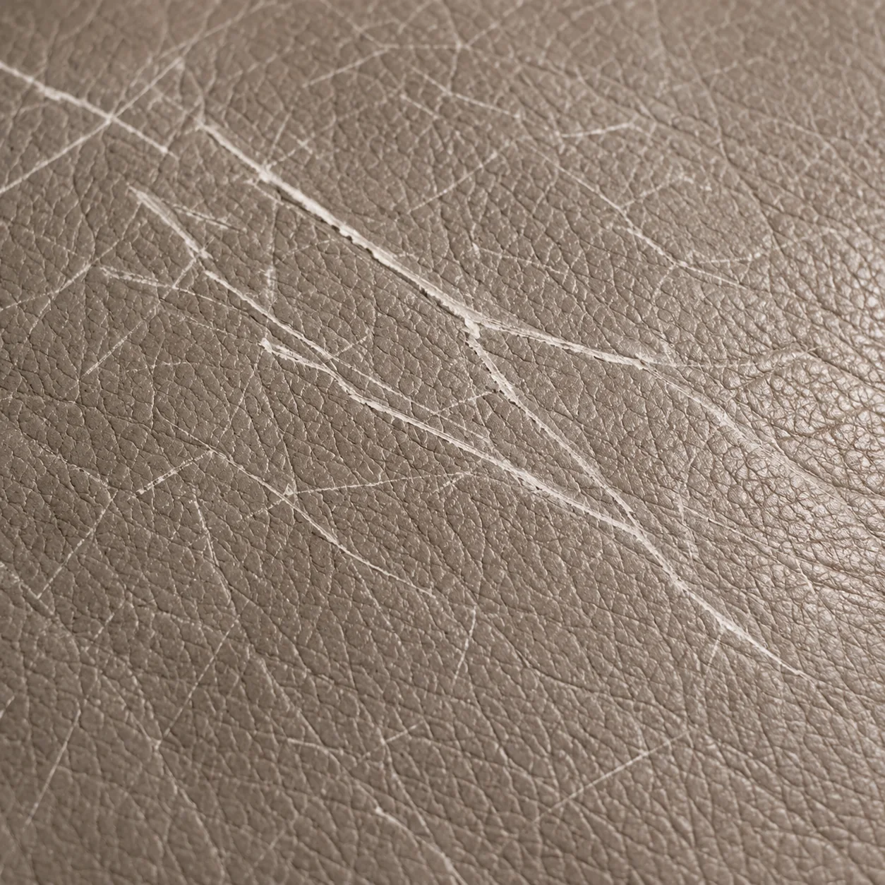 Pale scratch lines across a taupe leather panel