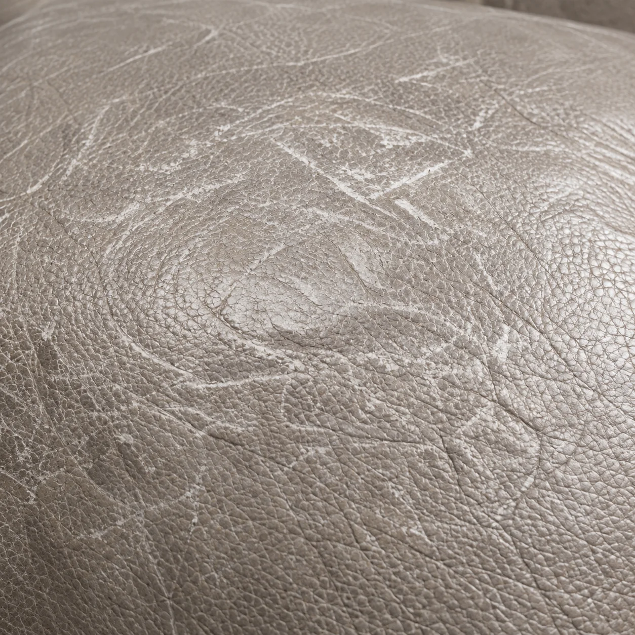 Broad scuffing across the crown of a taupe leather cushion