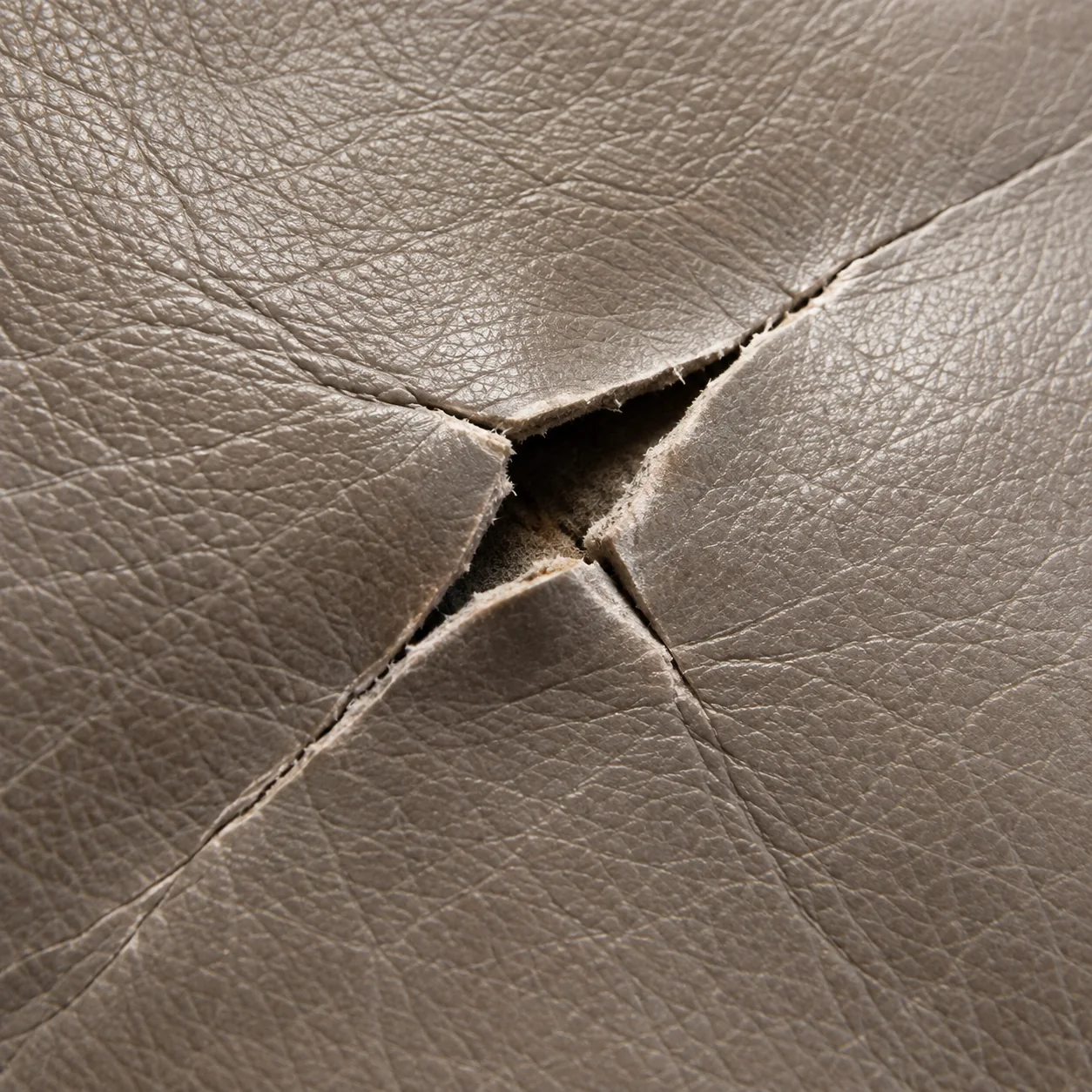 Open tear in a taupe leather panel with the backing showing