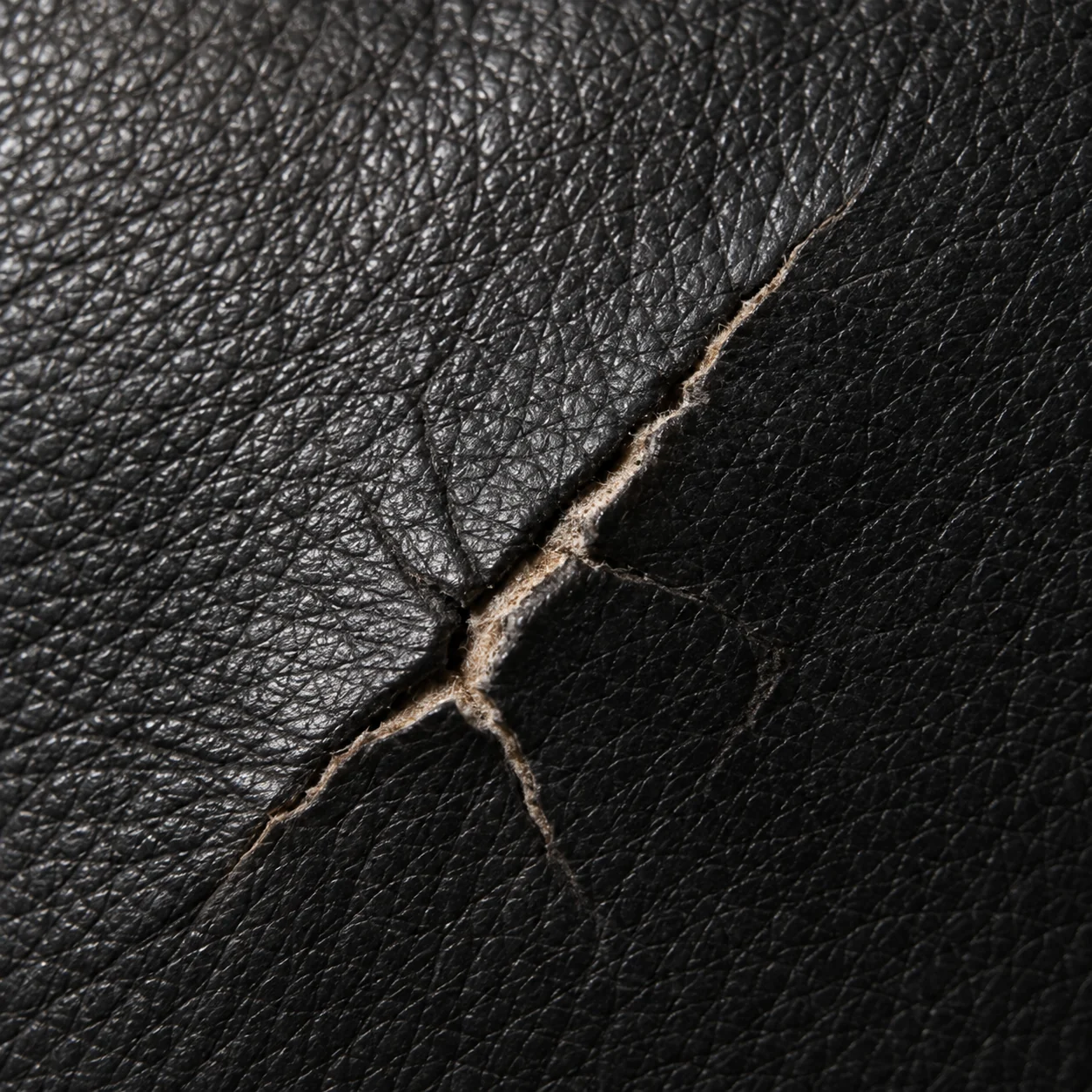 Black leather cracked through the finish to the pale fibres beneath