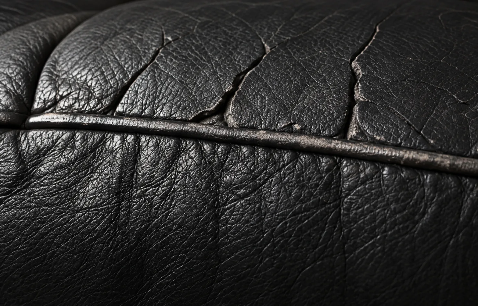 Black leather cracking open along a piped seam edge, before crack repair