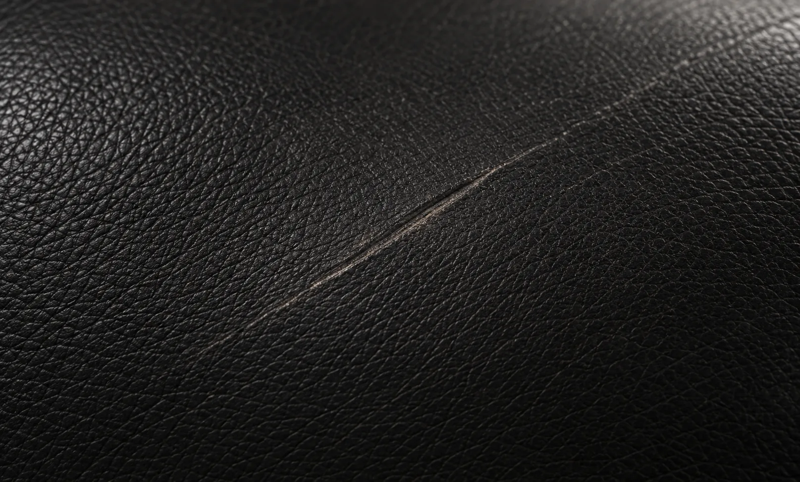 A fine scratch drawn across black leather before scratch repair