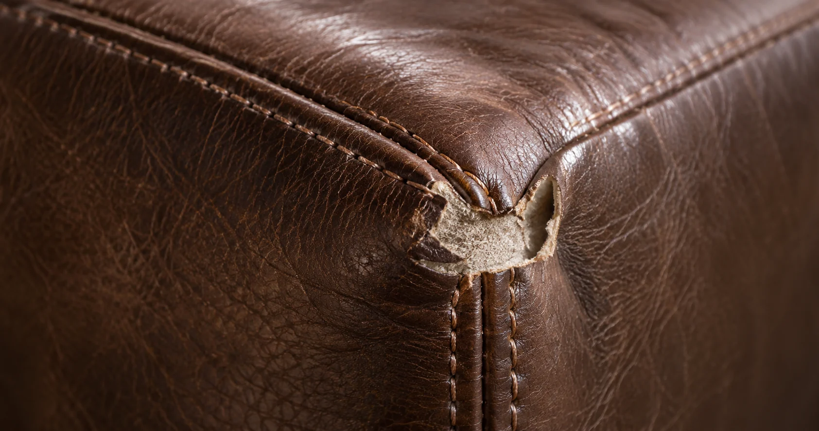 Corner of a brown leather bed where the finish has been rubbed thin along the edge