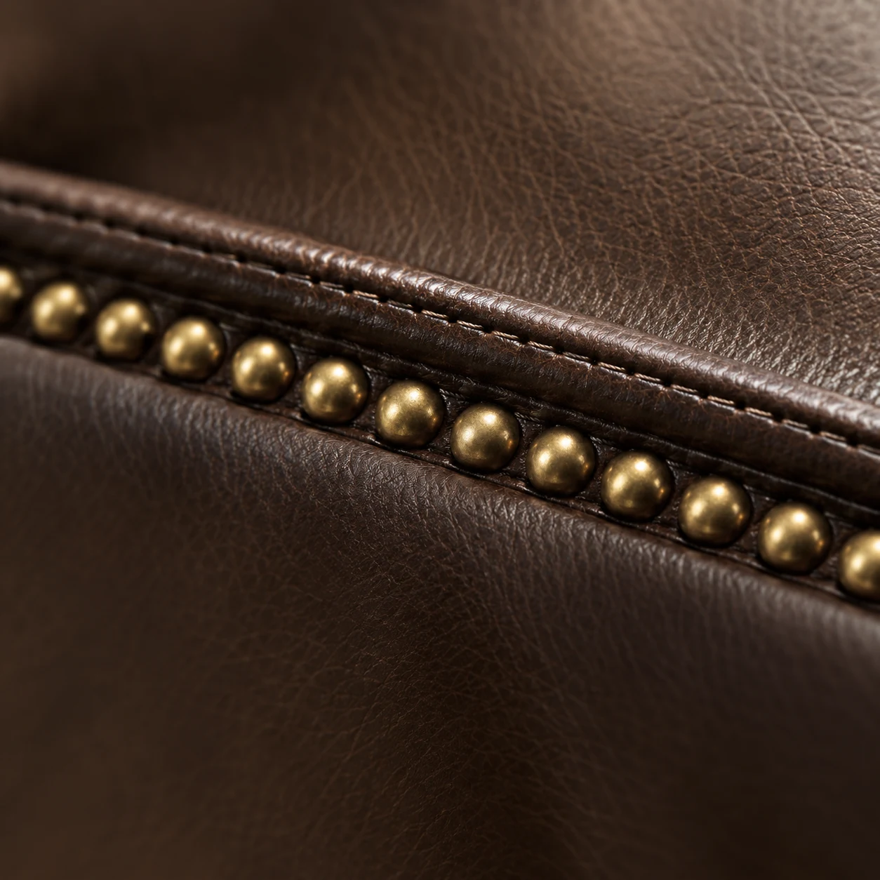 Brown leather chair arm with a close-set row of brass nailhead trim