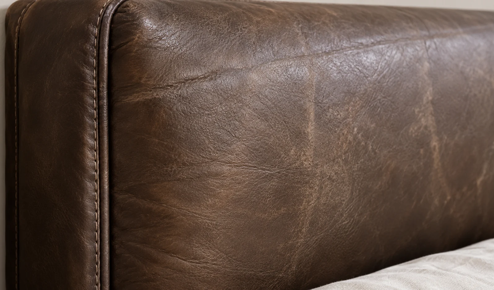 Sound top rail of a brown leather headboard seen at an angle