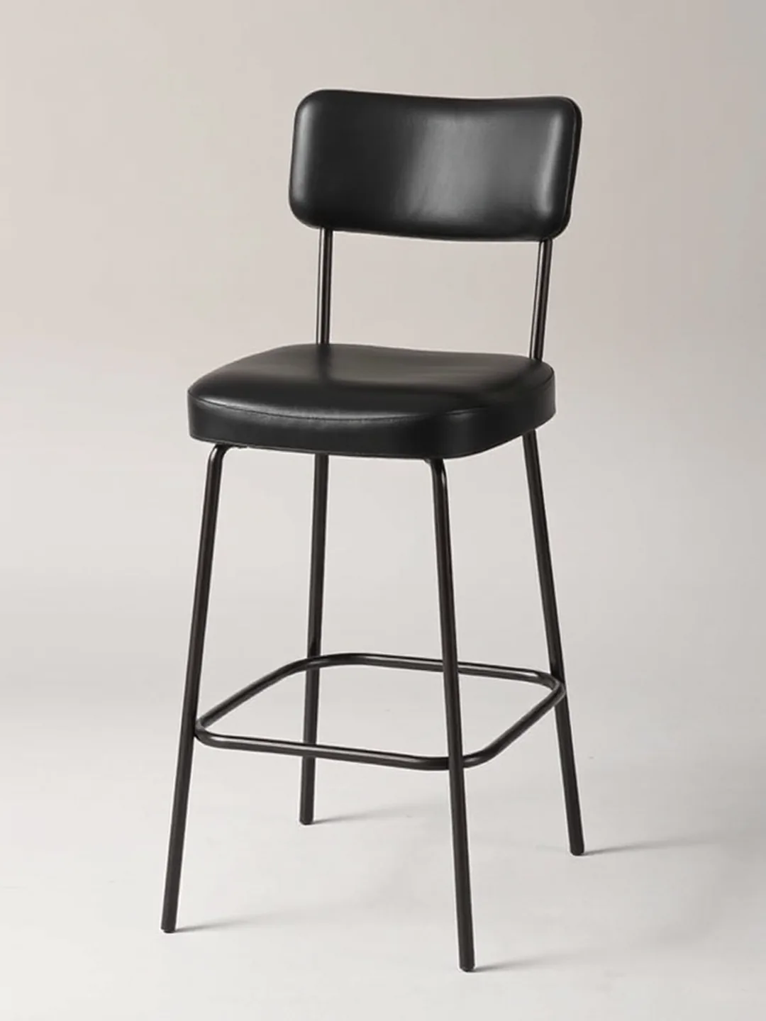 A low counter-height upholstered stool with a black leather seat and short back, side view