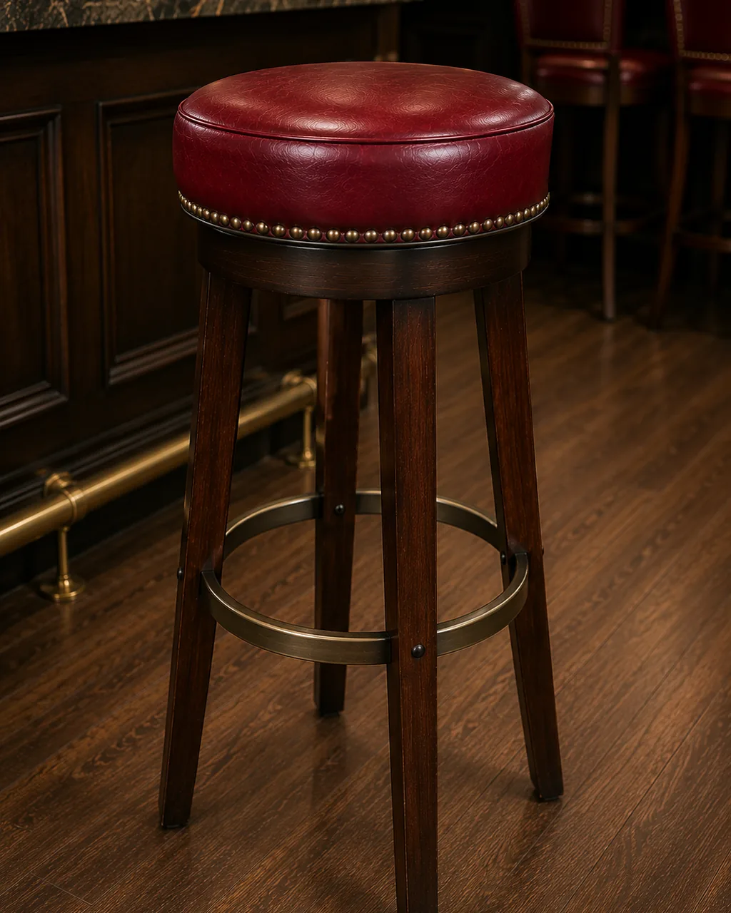 A backless round bar stool in red leather at a bar counter with a brass foot rail