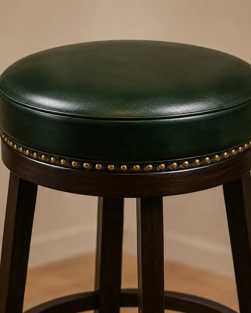 A round pad bar stool in green leather with a studded rim, on a dark timber column