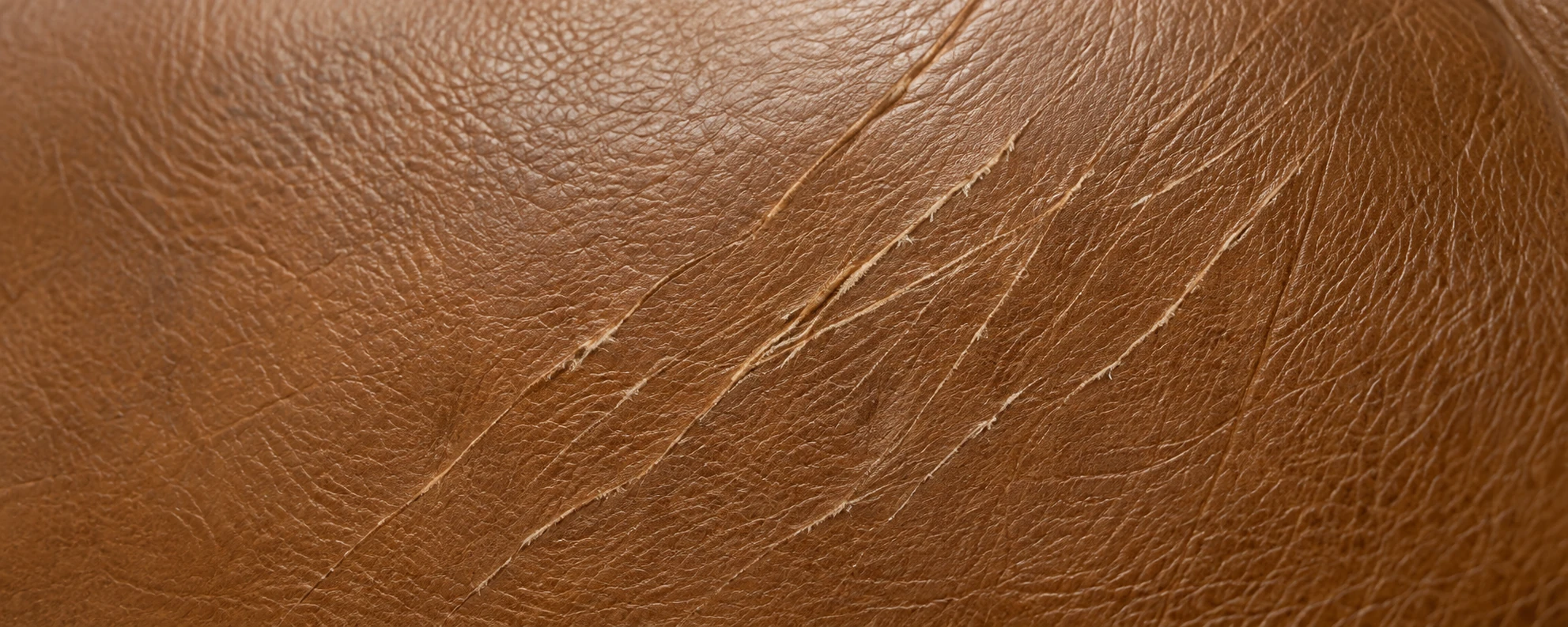 Tan leather panel before cat scratch leather repair, with pale claw drag lines running diagonally across it
