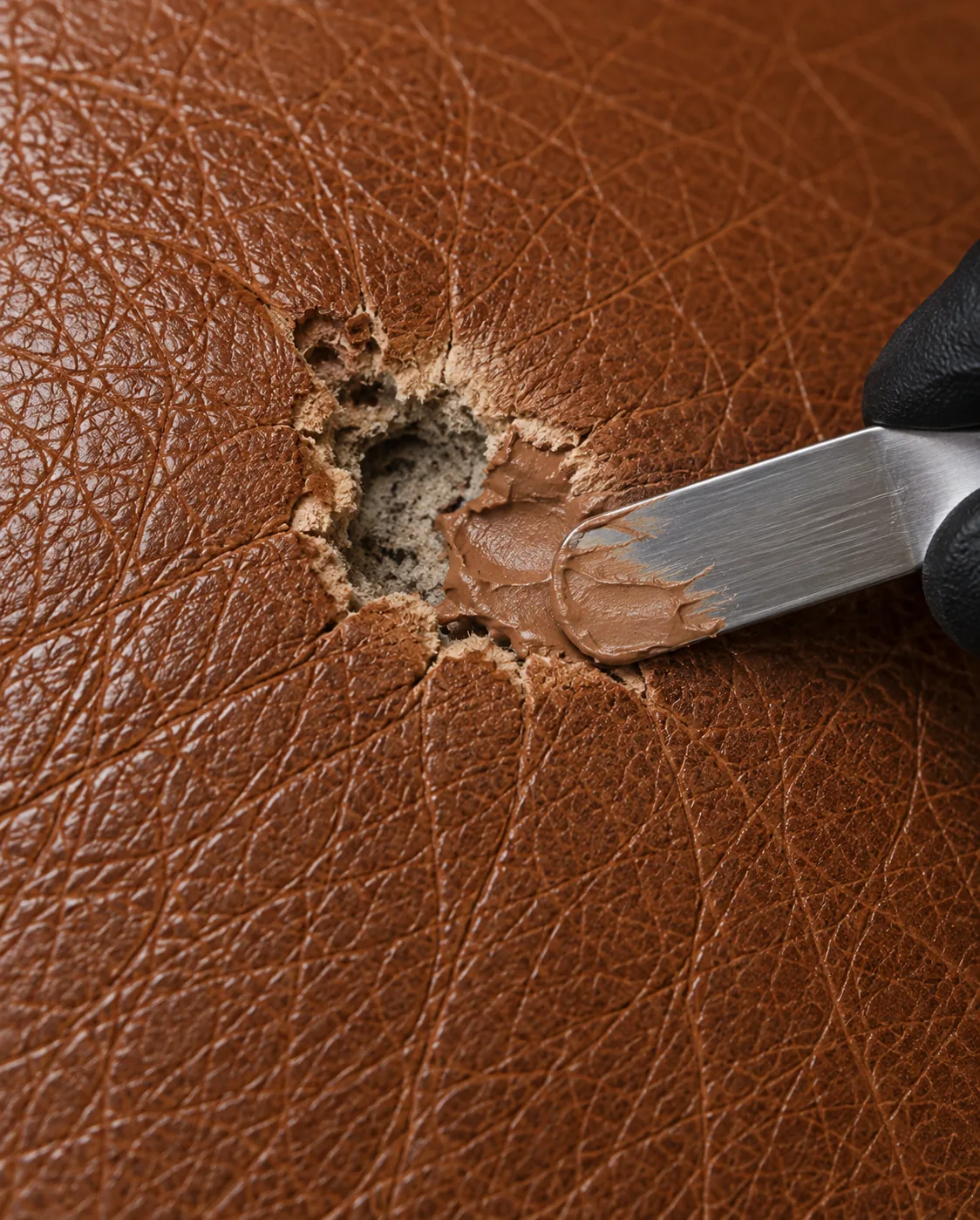 Scalpel paring the carbonised edge of a cigarette burn back to sound leather