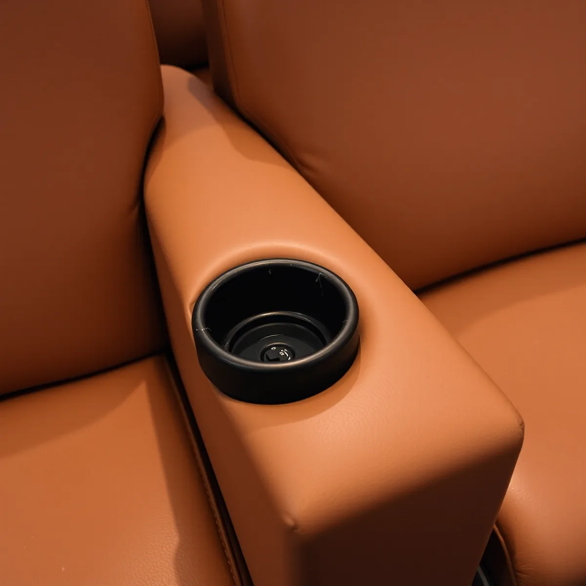The shared console arm between two tan brown leather cinema recliners, with a moulded cup holder set into its scuffed top