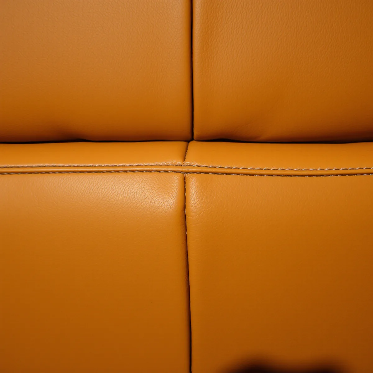 Close view of the tailored junction where the padded back of a tan brown leather cinema recliner meets its seat cushion, stitching and creasing visible across the fold line