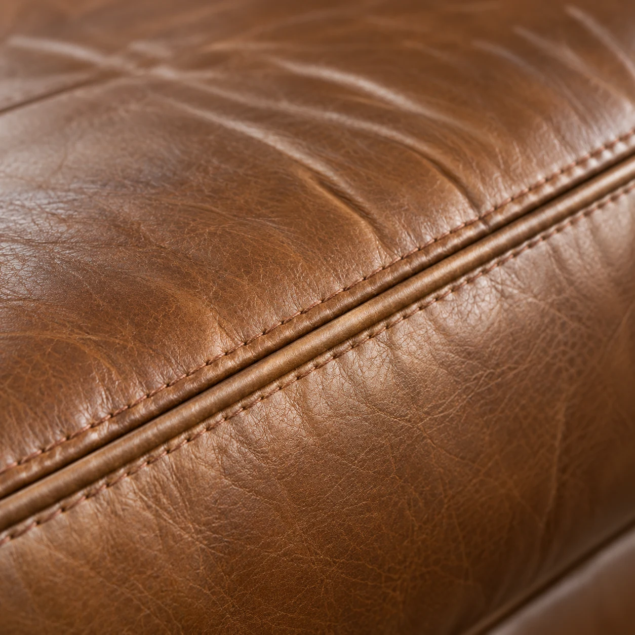 Welted seam running along a cognac leather sectional cushion