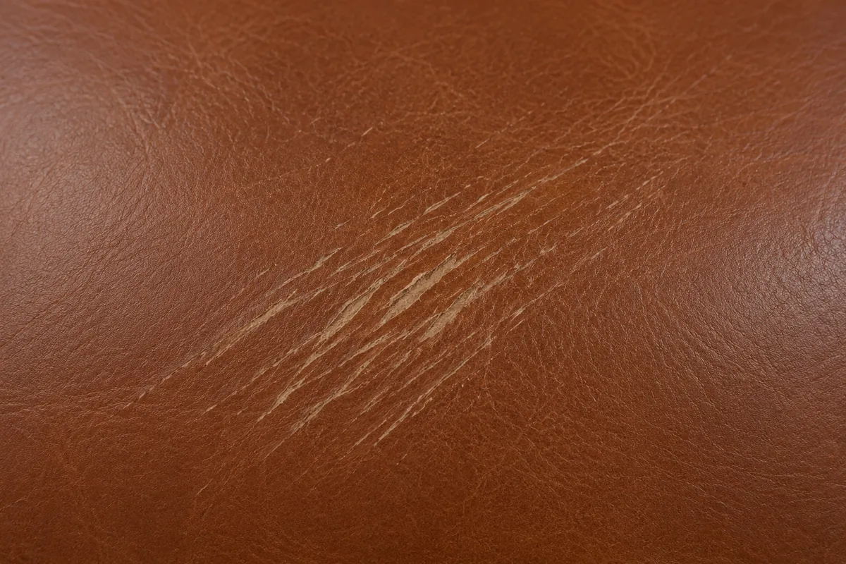 Close-up of a scratch on brown leather that has cut through the colour to a paler layer beneath