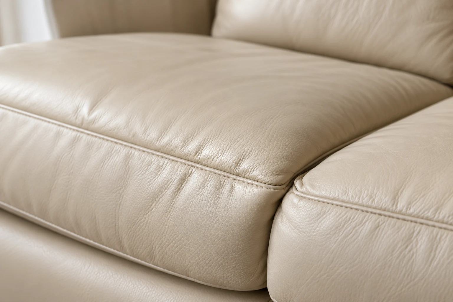 Two cream leather couch cushions meeting at a seam, one sitting lower than the other