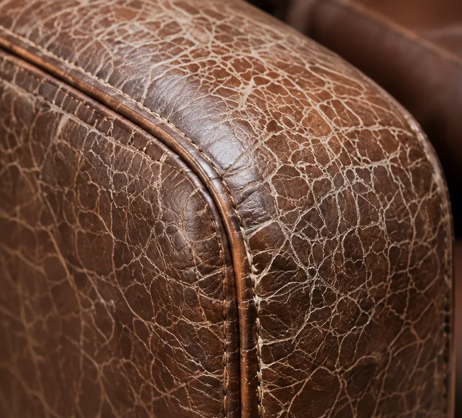 Brown leather sofa arm with dry surface cracking across the roll before treatment