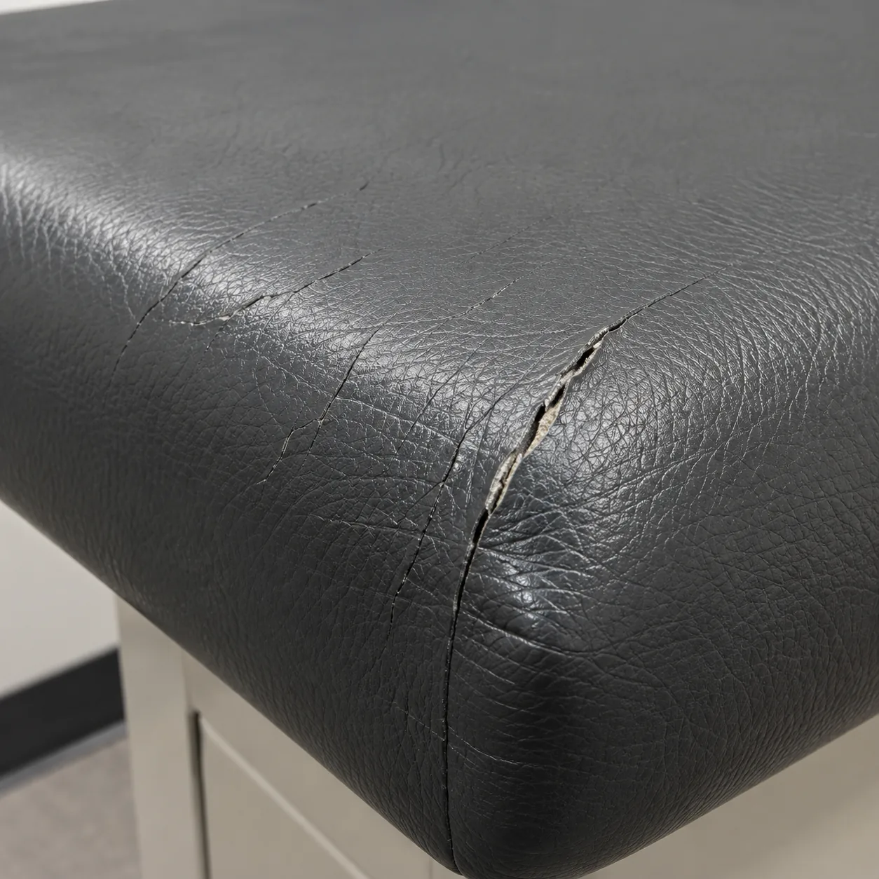 Cracked charcoal vinyl splitting at the corner of an exam table pad