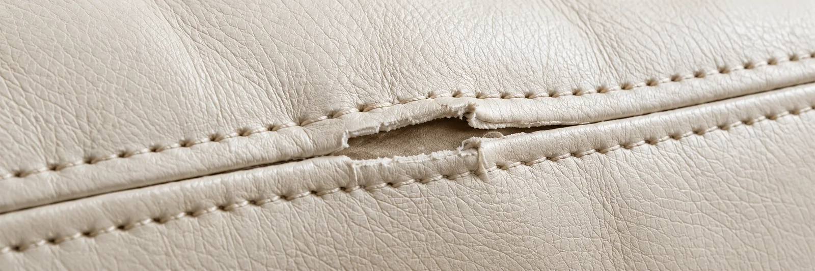 A seam pulling open where two cream leather panels meet