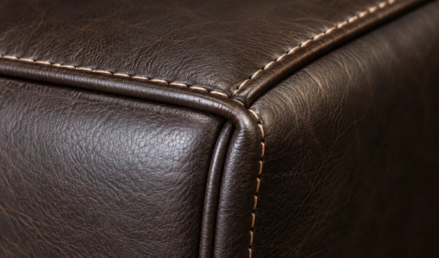 Corner of a dark brown leather bed where the piping meets the stitched panel edge