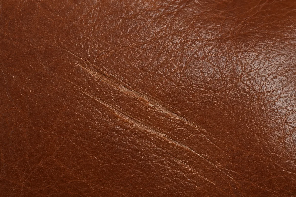 Close-up of a deep scratch gouged into brown leather, past the colour and into the hide