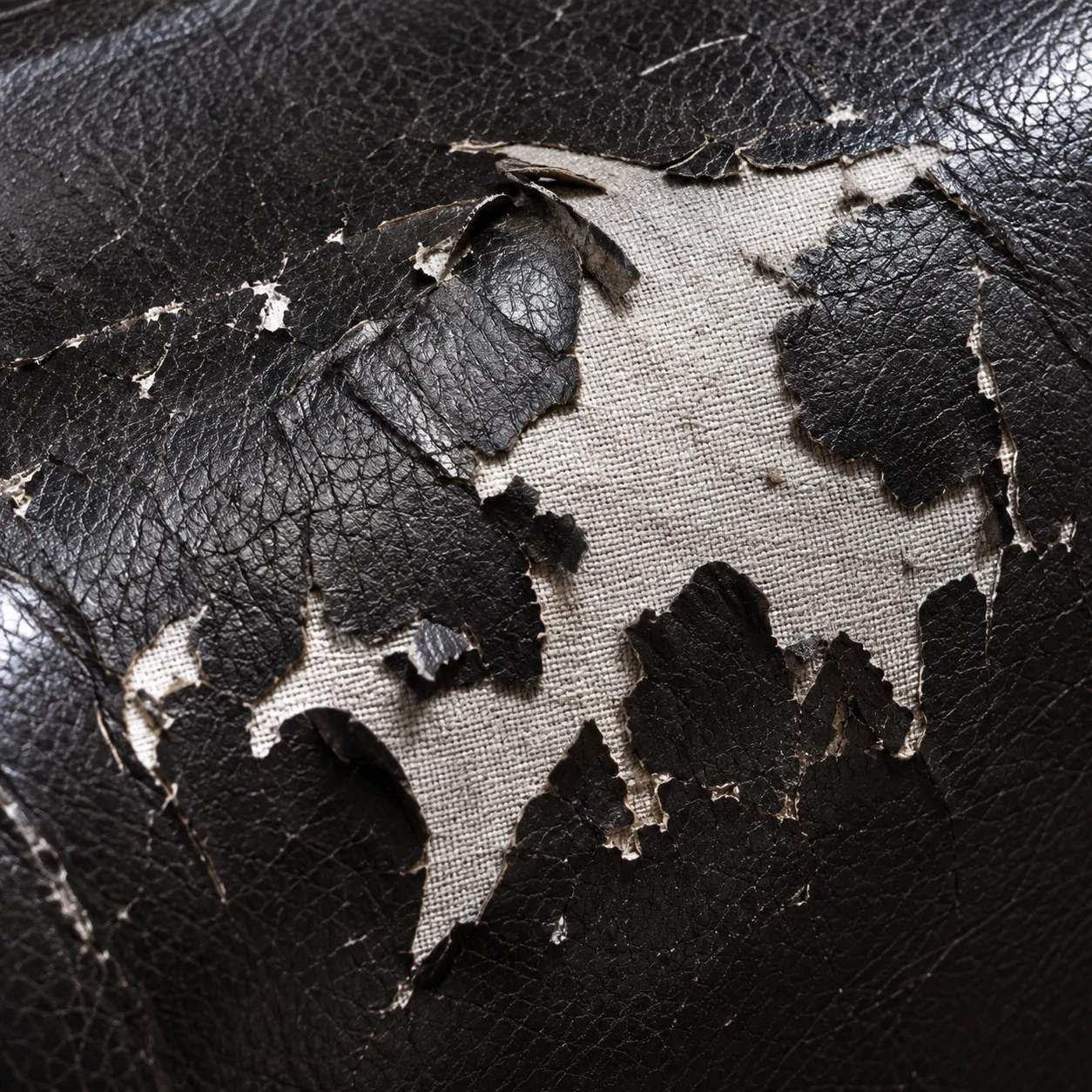 Black bonded leather peeled away from its fabric backing on a massage chair panel